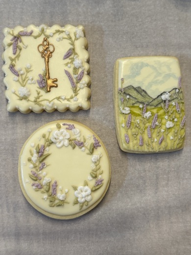 Lavender sugar cookies with a gold key, blossom wreath, and painted mountain field
